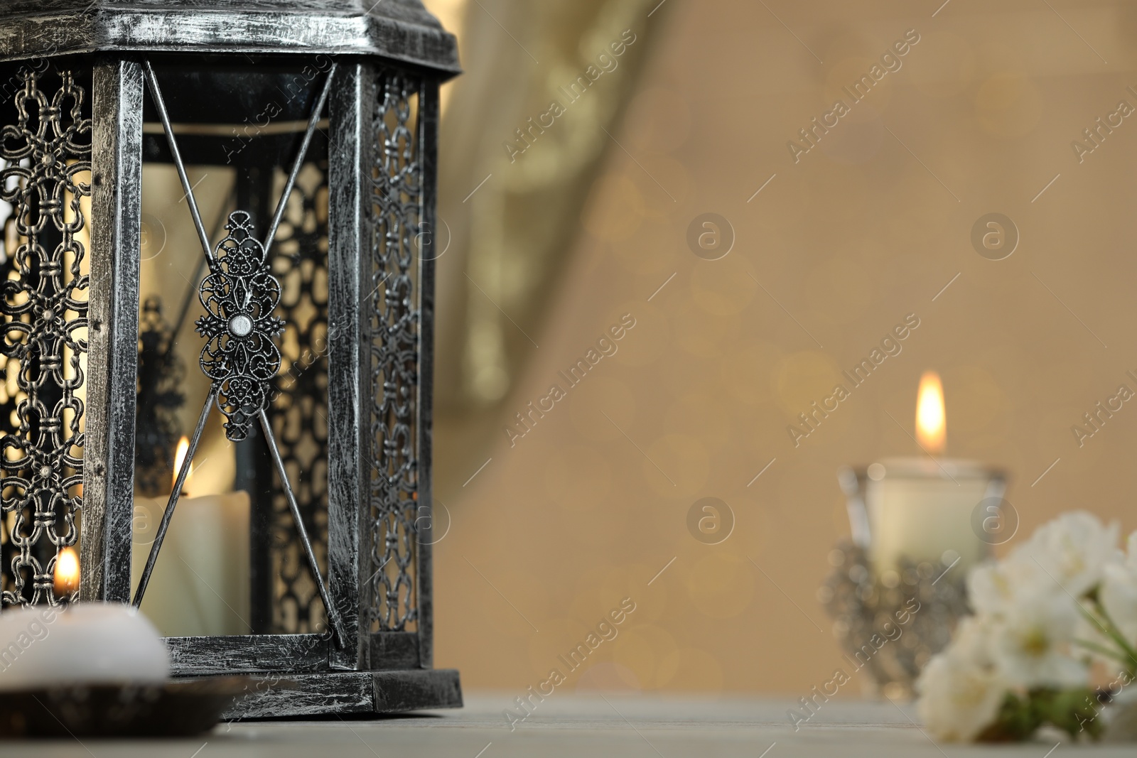 Photo of Arabic lantern and burning candles on table against blurred lights