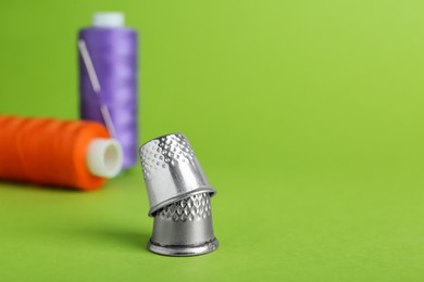 Photo of Thimbles and spools of sewing threads with needle on green background, closeup. Space for text