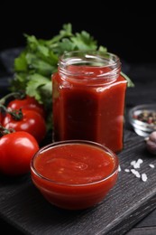 Photo of Delicious ketchup and products on black wooden table, closeup. Tomato sauce