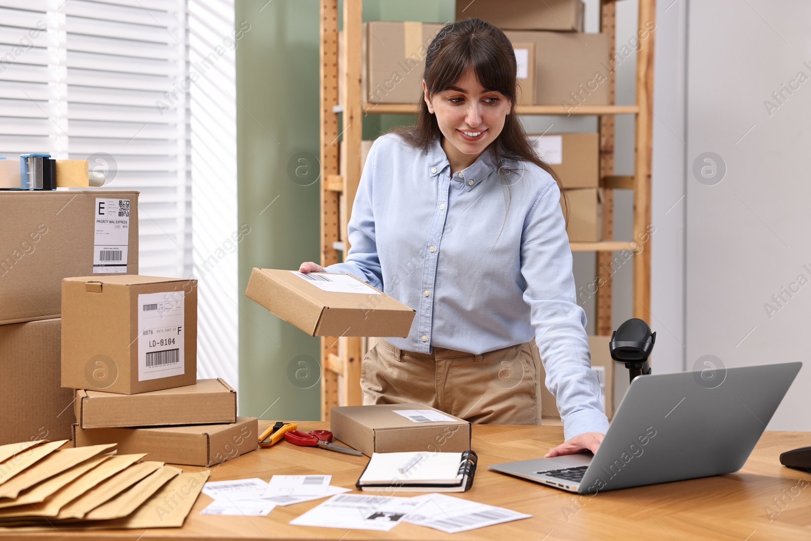 Photo of Parcel packing. Post office worker using laptop at wooden table indoors