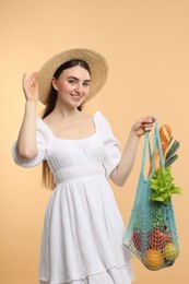 Woman with string bag of fresh vegetables and baguette on beige background