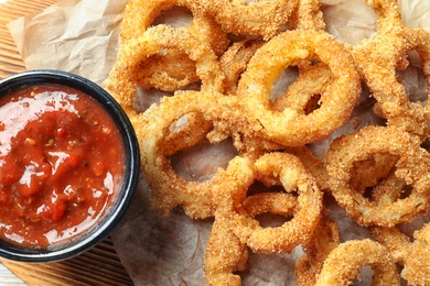 Photo of Homemade crunchy fried onion rings with tomato sauce, top view