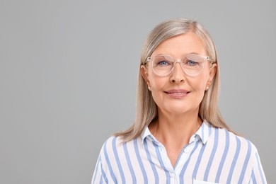 Photo of Portrait of beautiful middle aged woman in eyeglasses on light grey background, space for text