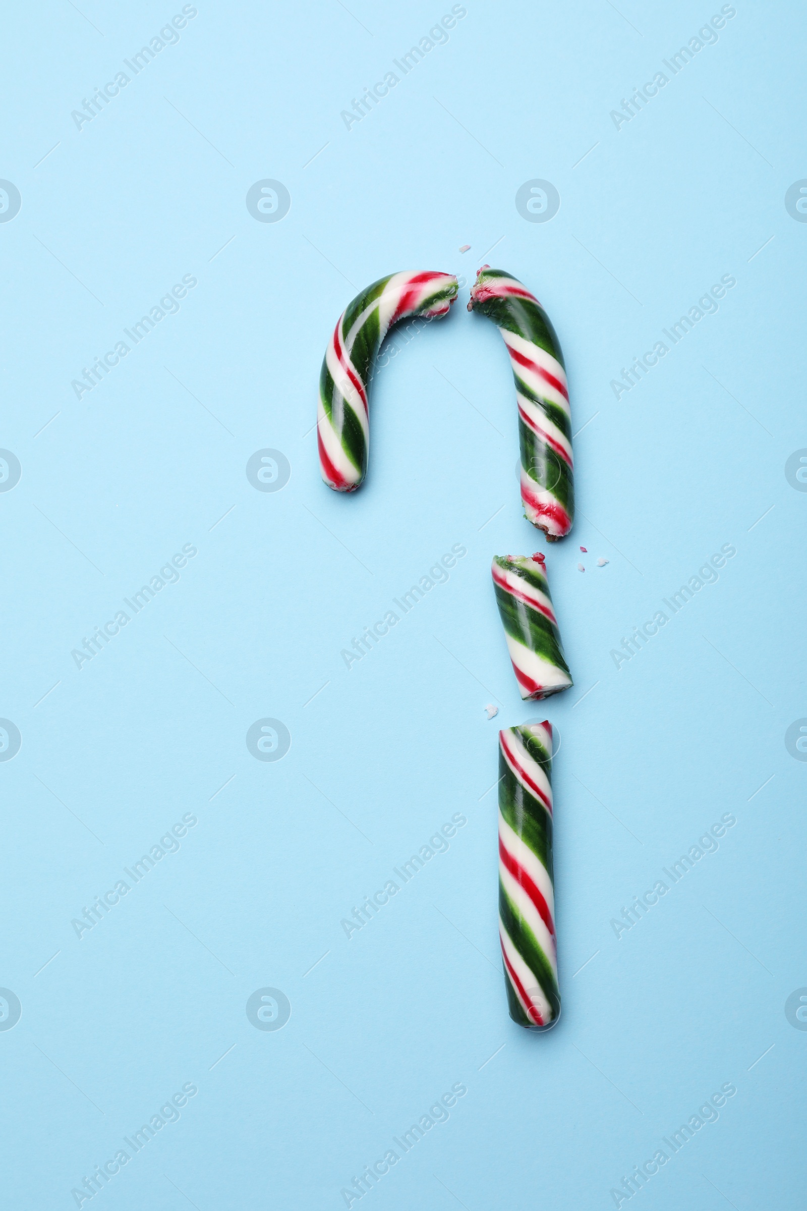 Photo of Broken sweet Christmas candy cane on light blue background, top view