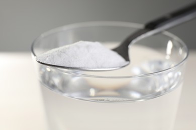 Photo of Glass of water and spoon with baking soda on color background, closeup