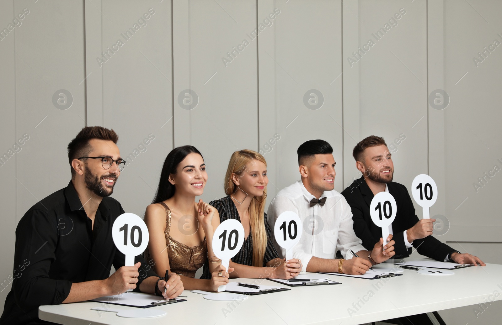 Photo of Panel of judges holding signs with highest score at table against light wall