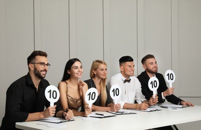 Panel of judges holding signs with highest score at table against light wall