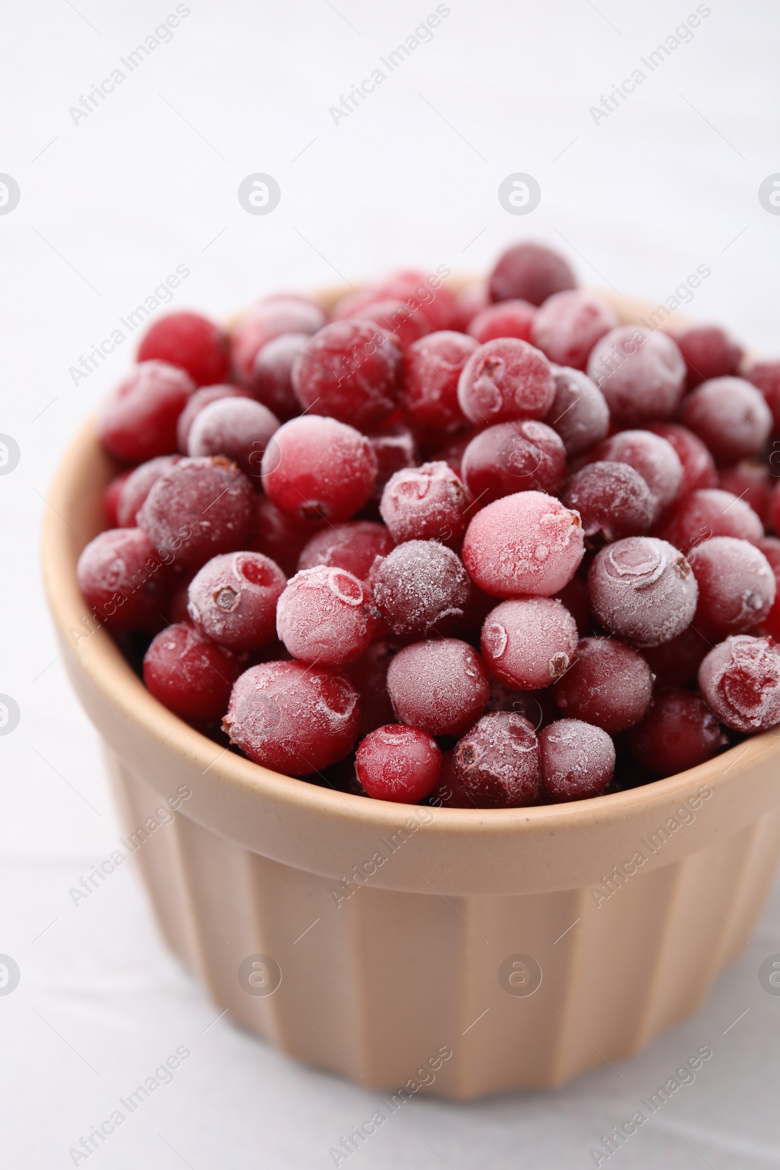 Photo of Frozen red cranberries in bowl on white table, closeup