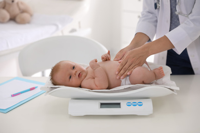 Photo of Doctor weighting cute baby in clinic, closeup. Health care