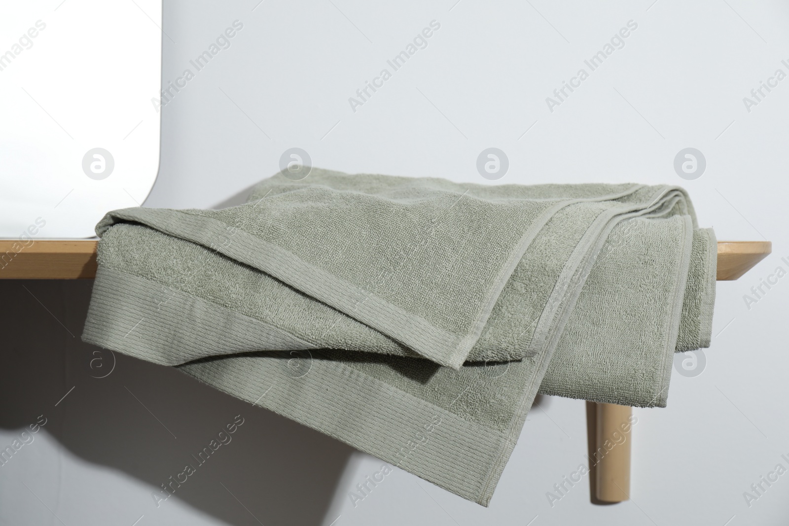 Photo of Green terry towel on wooden shelf near white wall