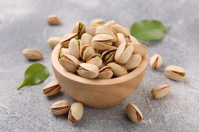 Delicious pistachios in bowl on grey textured table