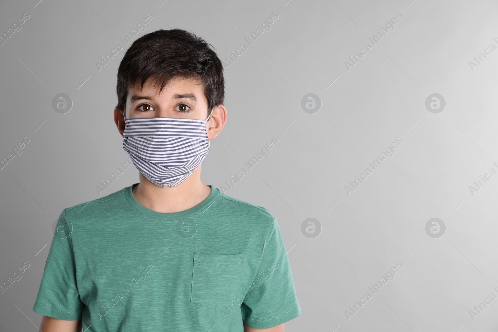 Photo of Boy wearing protective mask on light grey background, space for text. Child safety
