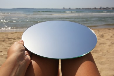 Photo of Woman with round mirror reflecting sky on beach, closeup