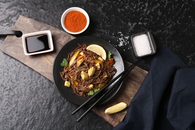 Photo of Stir-fry. Tasty noodles with vegetables and meat served on dark textured table, flat lay