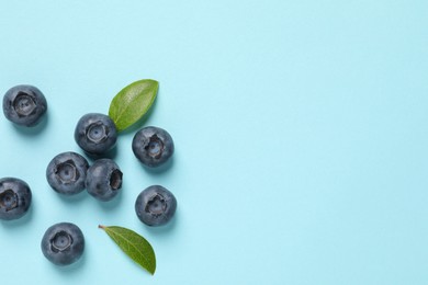 Photo of Tasty fresh blueberries with green leaves on light blue background, flat lay. Space for text