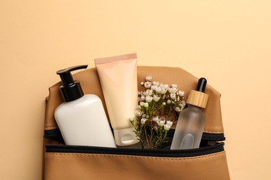 Photo of Preparation for spa. Compact toiletry bag with different cosmetic products and flowers on beige background, top view