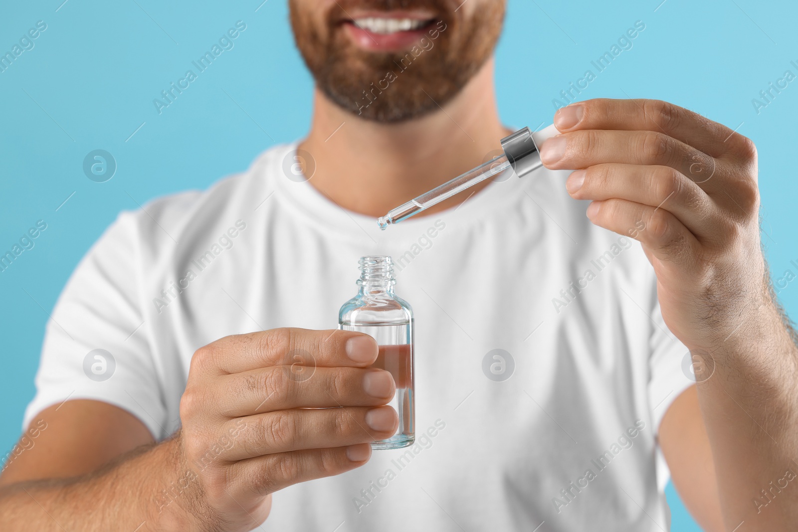 Photo of Smiling man with cosmetic serum on light blue background, selective focus