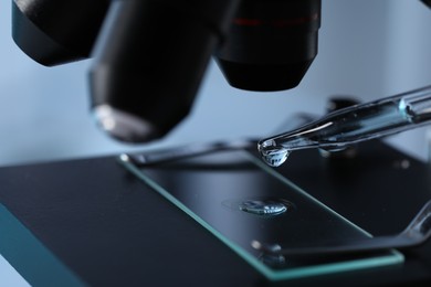 Photo of Dropping light blue liquid from pipette on glass slide in laboratory, closeup