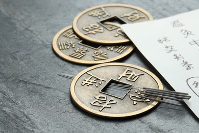Photo of Acupuncture needles, Chinese coins and paper with characters on grey textured table, closeup