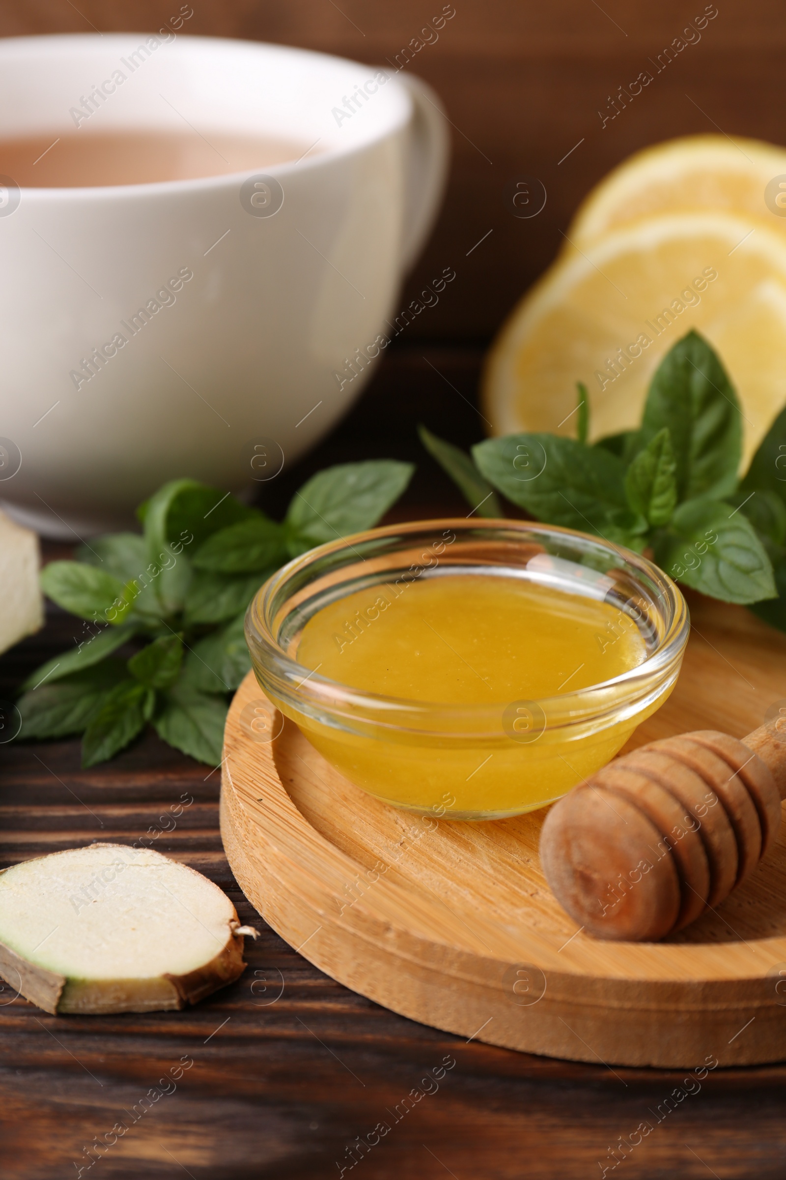 Photo of Bowl with honey for tea, lemon, mint and ginger on wooden table