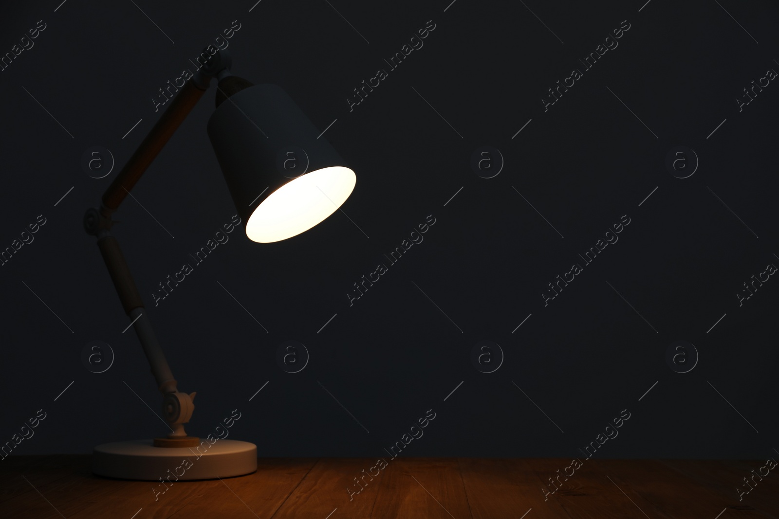 Photo of Stylish modern desk lamp on wooden table at night, space for text