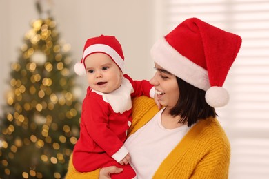 Happy young mother with her cute baby against blurred festive lights. Winter holiday