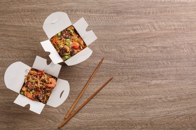Boxes of wok noodles with seafood and chopsticks on wooden table, flat lay. Space for text