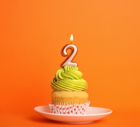 Birthday cupcake with number two candle in saucer on orange background