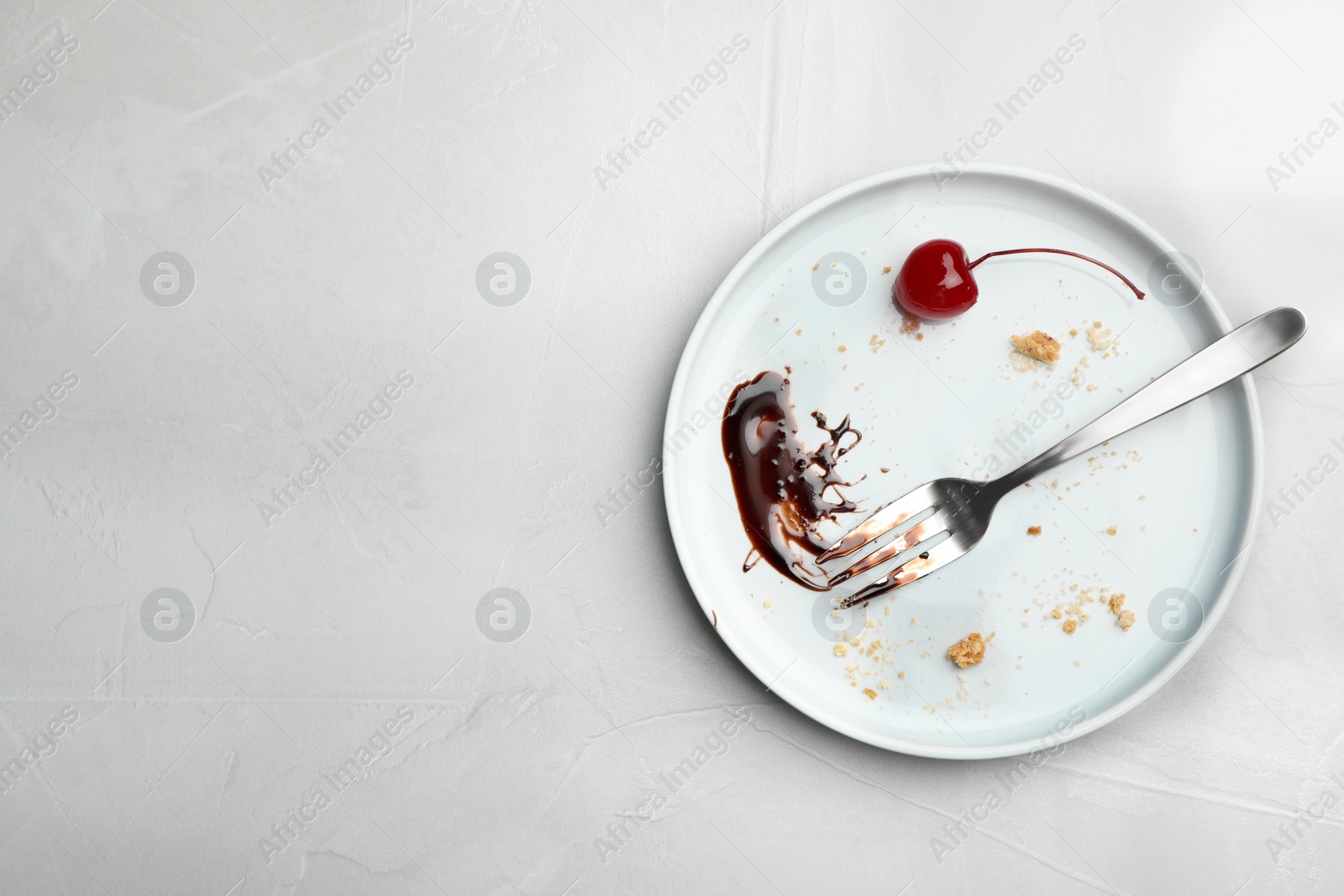 Photo of Dirty plate with food leftovers, fork and canned cherry on grey background, top view. Space for text