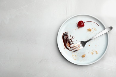 Dirty plate with food leftovers, fork and canned cherry on grey background, top view. Space for text