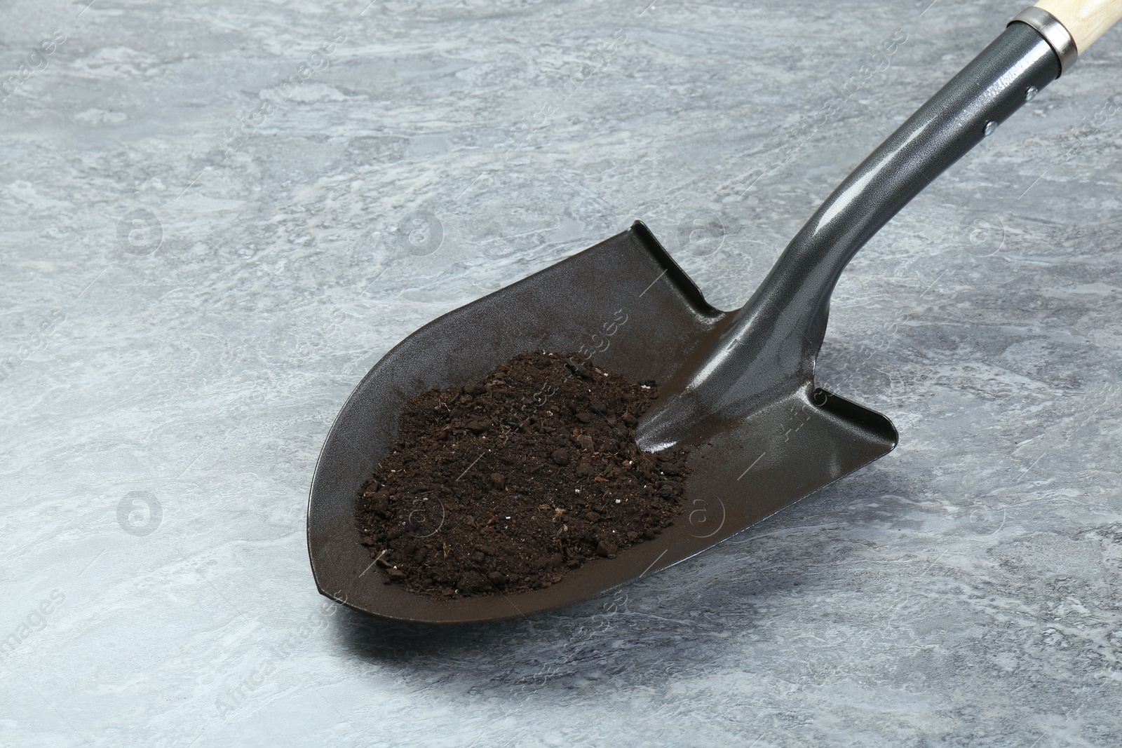 Metal shovel with fertile soil on gray textured surface Photo of Metal shovel with fertile soil on gray textured surface