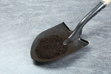 Photo of Metal shovel with fertile soil on gray textured surface