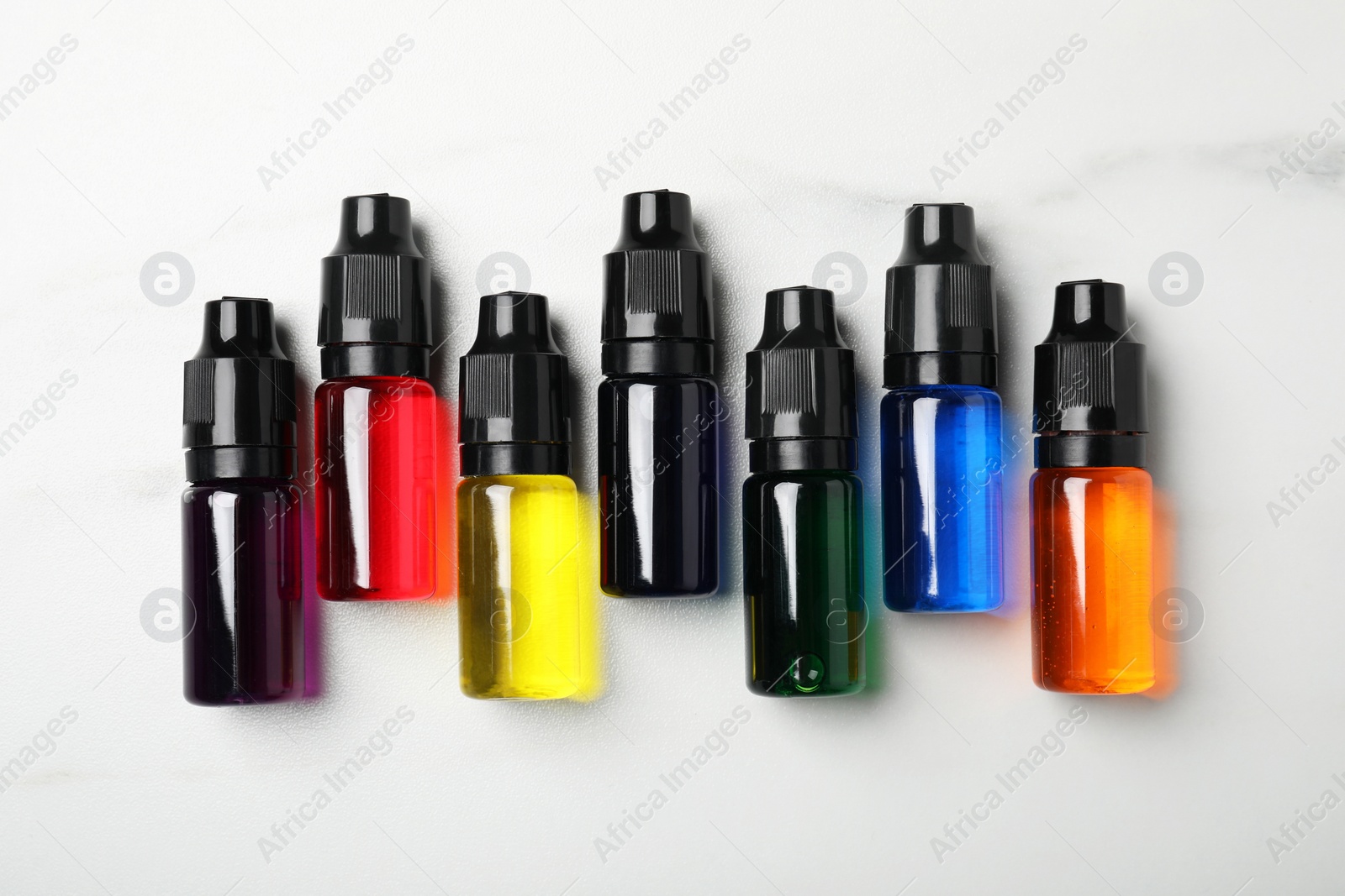 Photo of Bottles with different food coloring on white marble table, flat lay