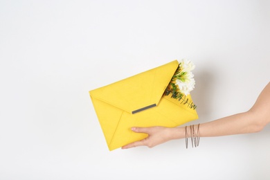 Photo of Woman with stylish clutch and spring flowers against light background, closeup