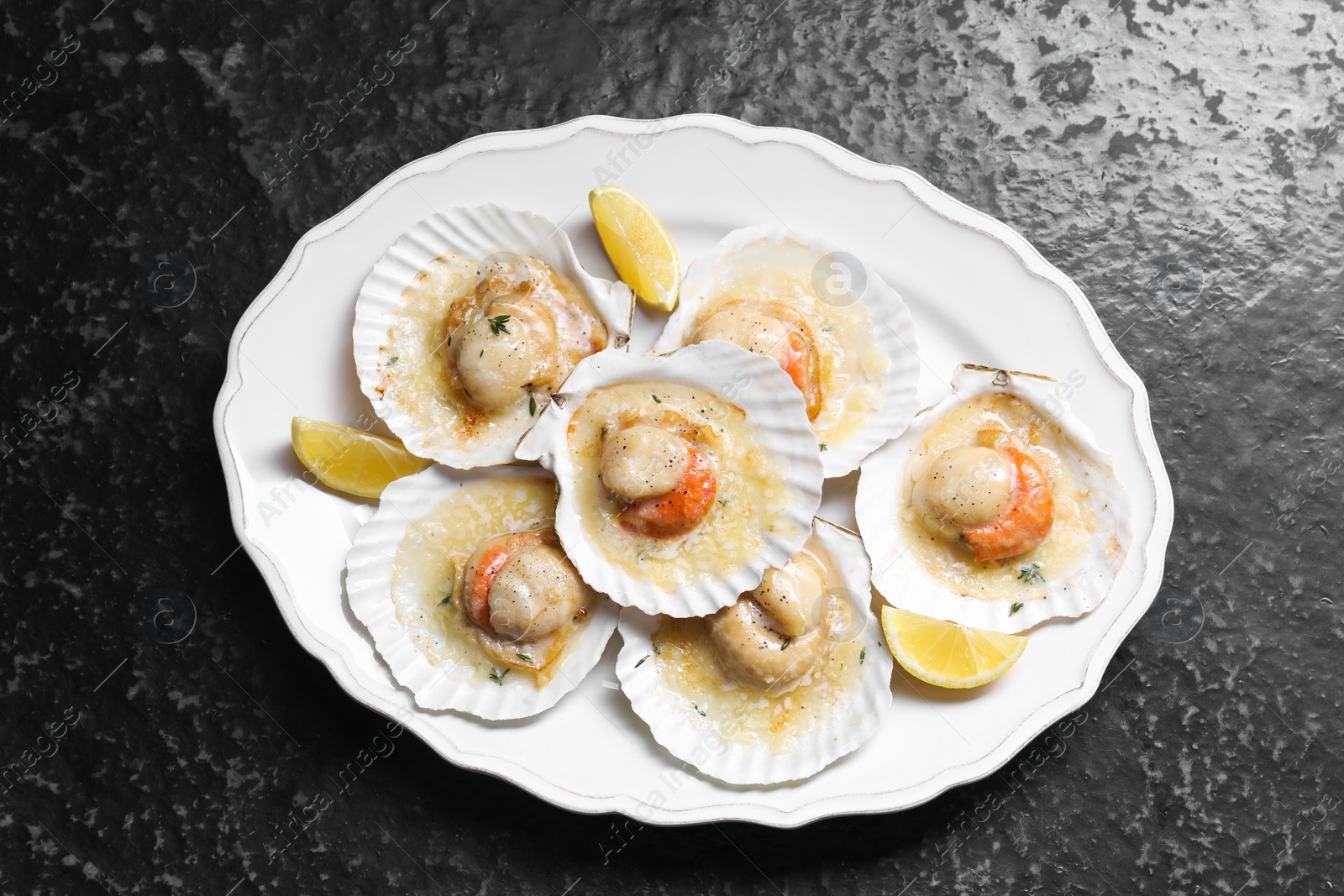 Photo of Fried scallops in shells and lemon on black textured table, top view