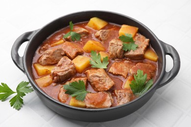 Delicious goulash in pot on white tiled table, closeup
