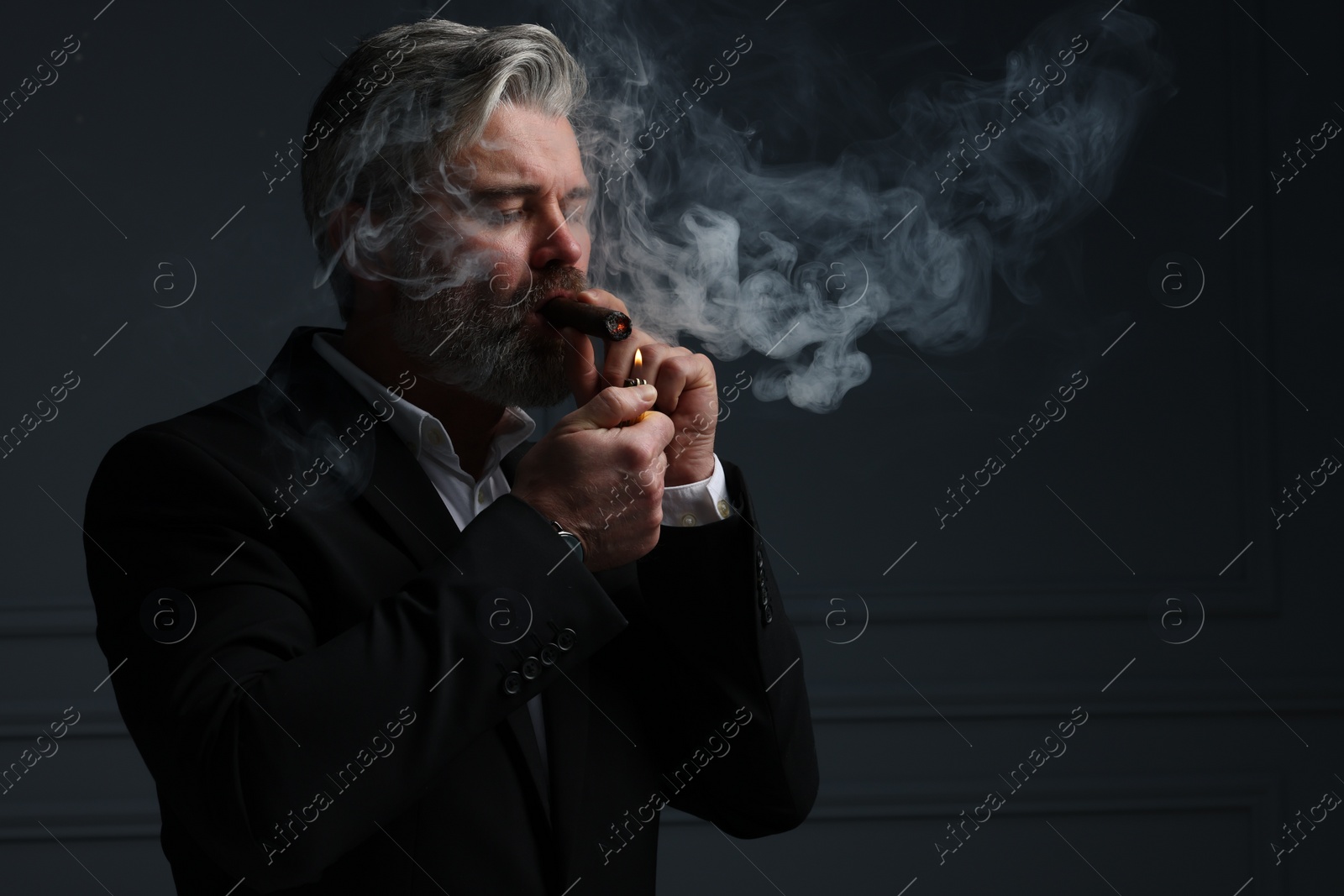 Photo of Bearded man lighting cigar on dark grey background. Space for text