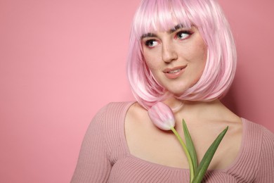 Photo of Beautiful woman with bright makeup, fake freckles and tulip on pink background. Space for text