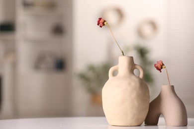 Vases with dried flowers on white table in room, space for text