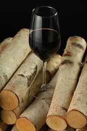 Photo of Red wine in wineglass on wooden logs against black background