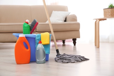 Mop and detergents on floor in living room, space for text. Cleaning service