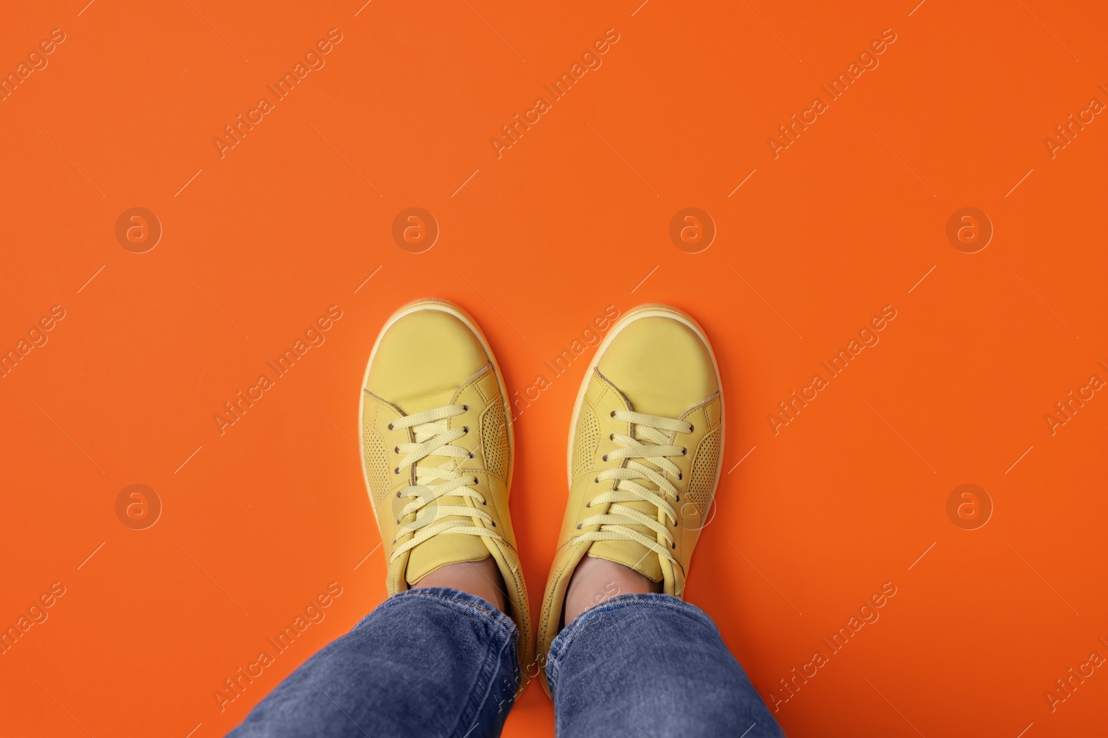 Photo of Woman in stylish sneakers on orange background, top view