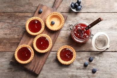 Photo of Tasty tartlets with jam on wooden background, top view