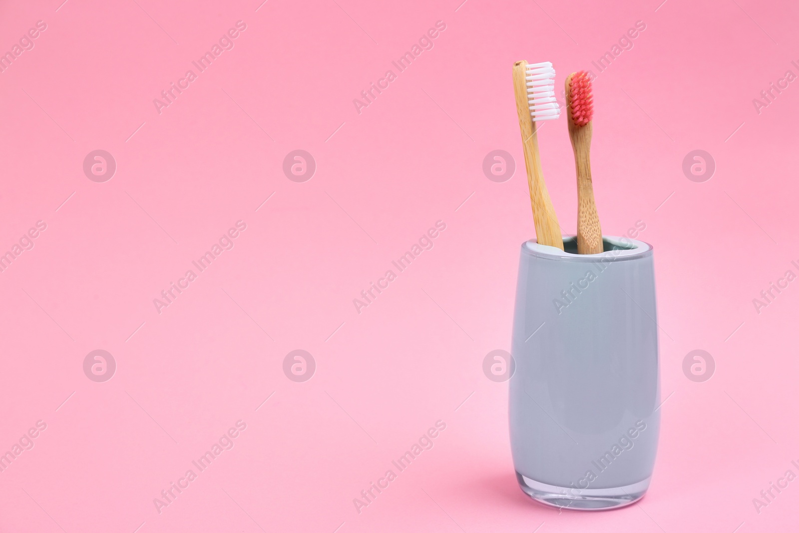 Photo of Toothbrushes made of bamboo in holder on pink background. Space for text