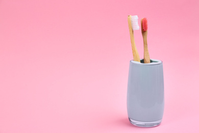 Photo of Toothbrushes made of bamboo in holder on pink background. Space for text