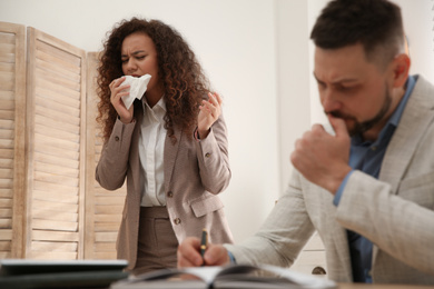 Sick African-American woman sneezing during meeting in office. Influenza virus