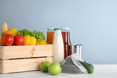 Photo of Crate with fresh vegetables and other products on white wooden table against light blue background