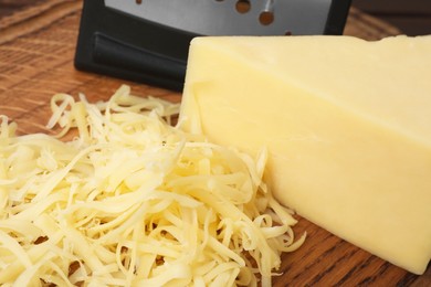 Photo of Grated and whole piece of cheese on wooden board, closeup