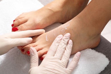 Pedicurist applying cream onto client`s foot after pedicure procedure in beauty salon, closeup