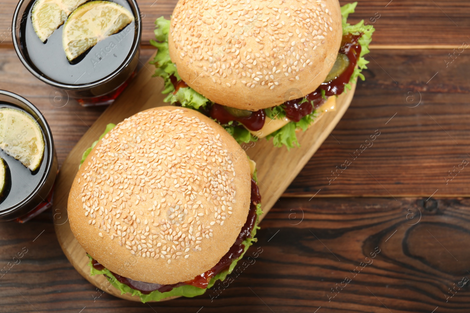 Photo of Delicious cheeseburgers and drinks on wooden table, top view. Space for text